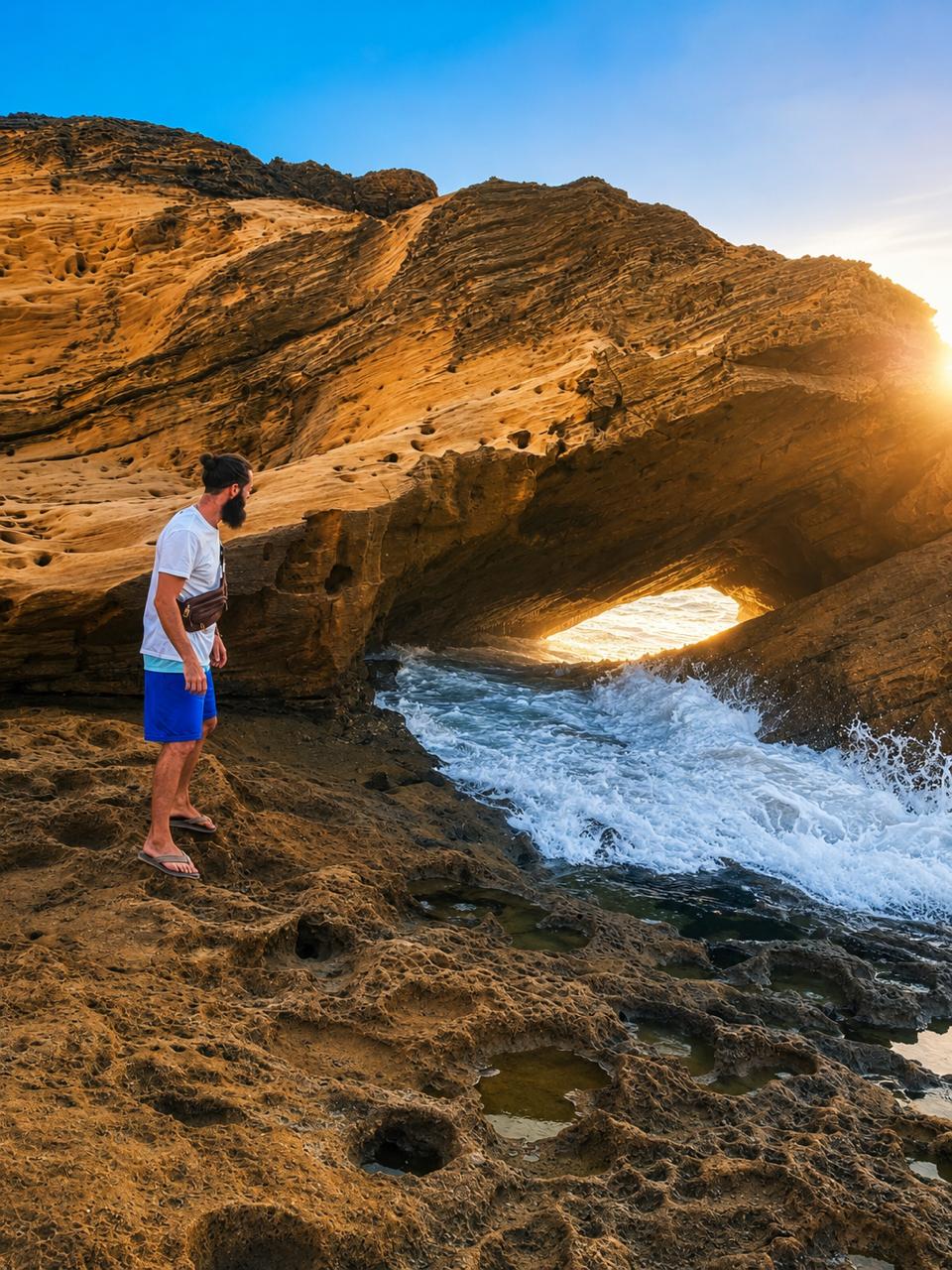 A man standing on a rocky beach near a waterfall.
