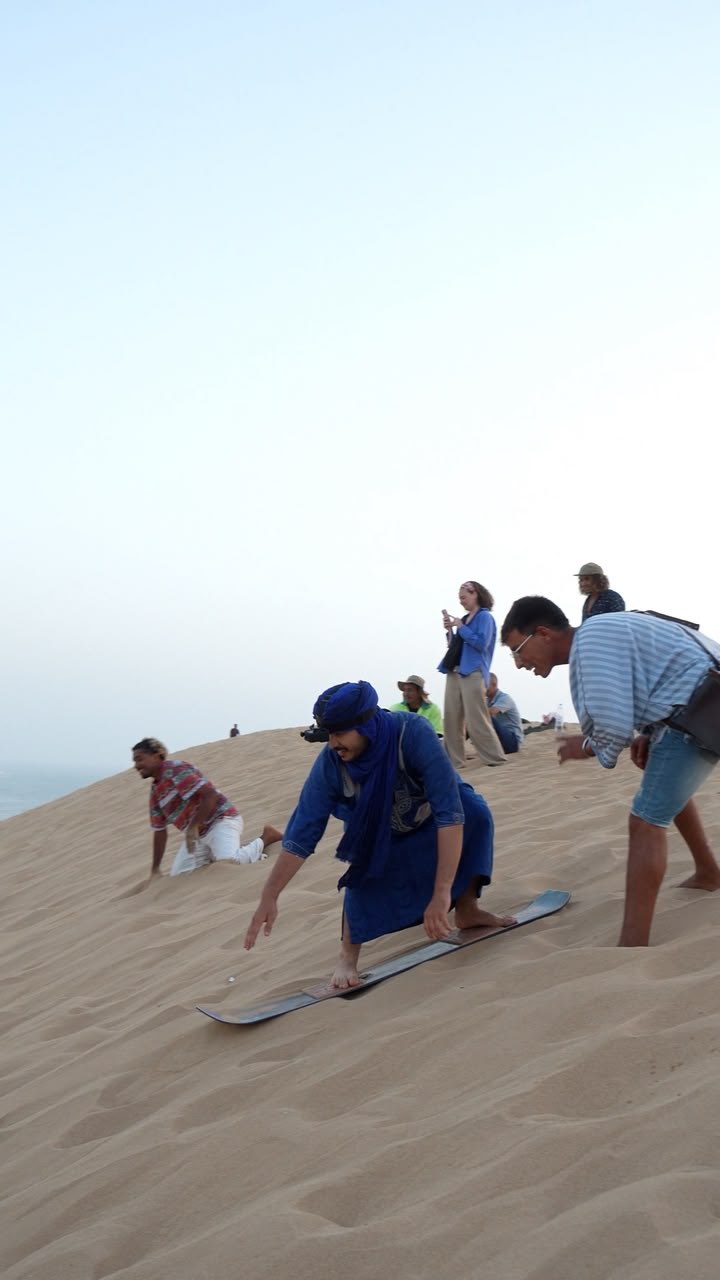 A man in a blue dress is riding a snowboard on a sandy beach. — Timlaline / Timlalin dunes quad tour photo, Agadir Morocco